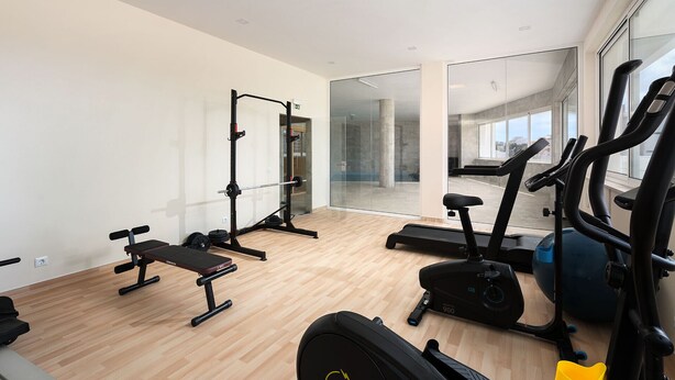 Un gimnasio moderno con equipo cardiovascular, estaciones de levantamiento de pesas y un espejo grande que refleja el espacio.