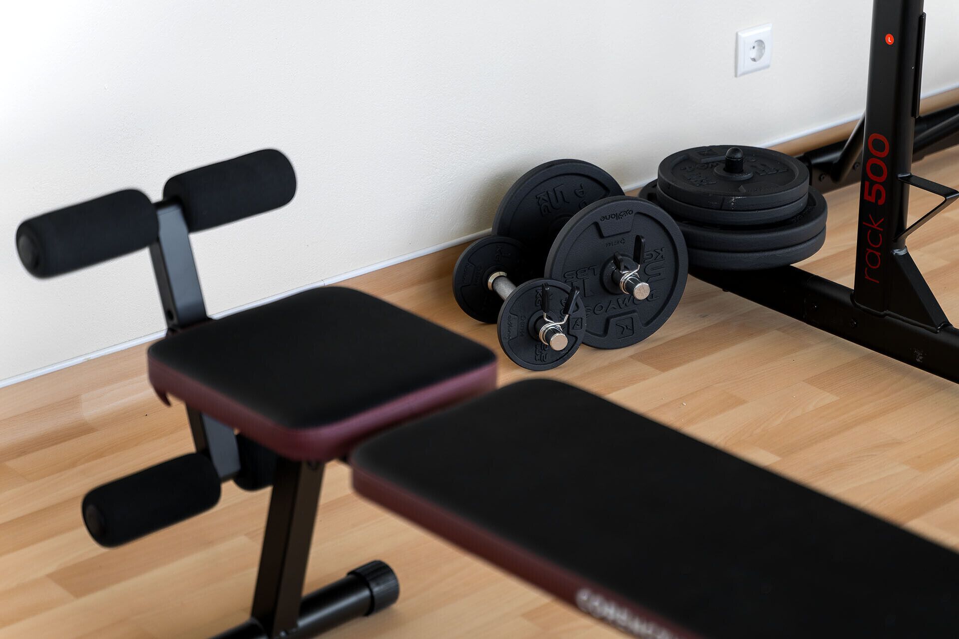 A gym with a bench, dumbbells, and a weight rack.