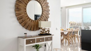 Un salon moderne doté d’un grand miroir rond, d’une table à manger avec des chaises, et offrant une vue sur la ville grâce à de grandes fenêtres.