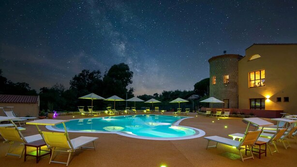 A nighttime swimming pool area with lounge chairs and umbrellas, under a starry sky. - Hotel with swimming pool in Arbus (Arbus)