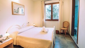 A hotel room with a bed, bedside table, lamp, and a chair near a window. - Hotel with swimming pool in Arbus (Arbus)