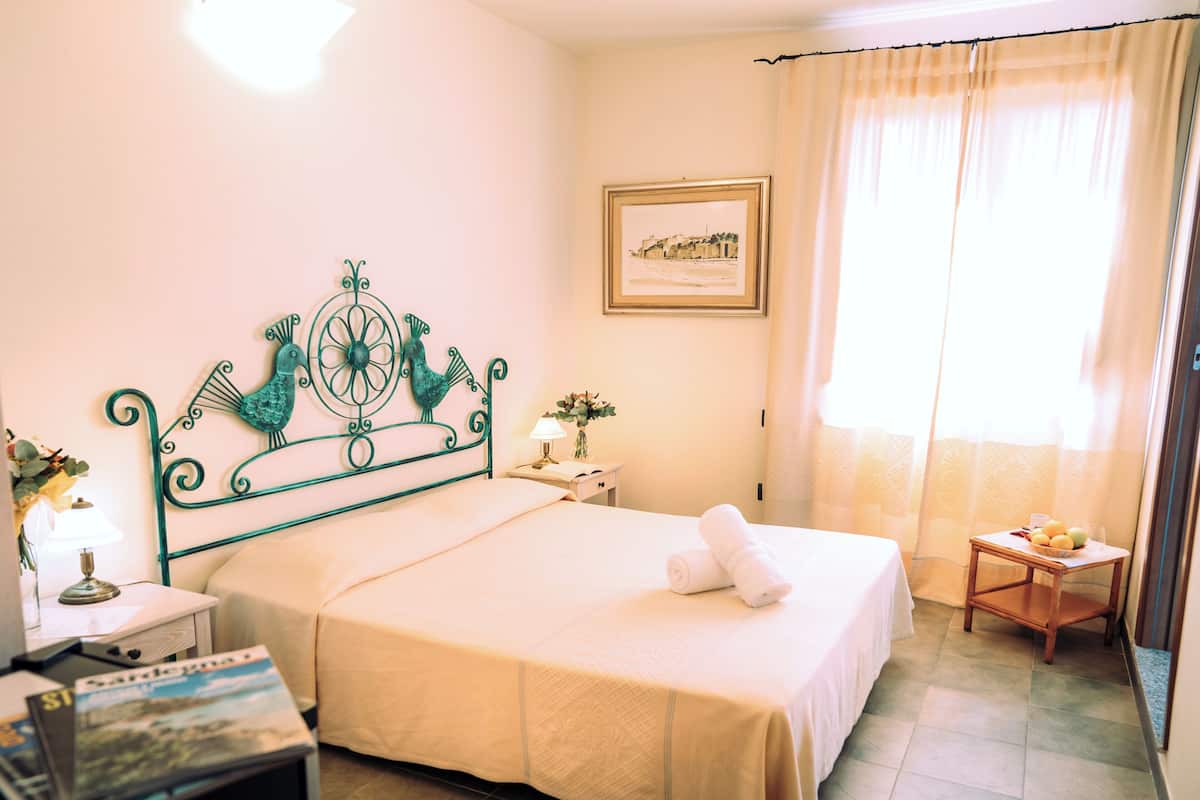 A hotel room with a bed, a nightstand, a lamp, a framed picture on the wall, and a window with curtains.