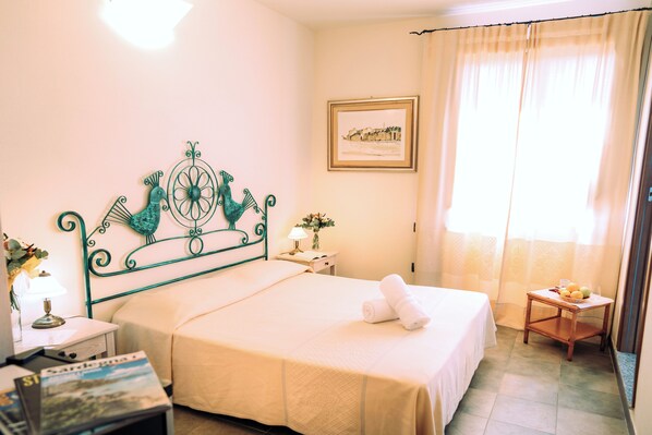 A hotel room with a bed, a nightstand, a lamp, a framed picture on the wall, and a window with curtains. - Hotel with swimming pool in Arbus (Arbus)