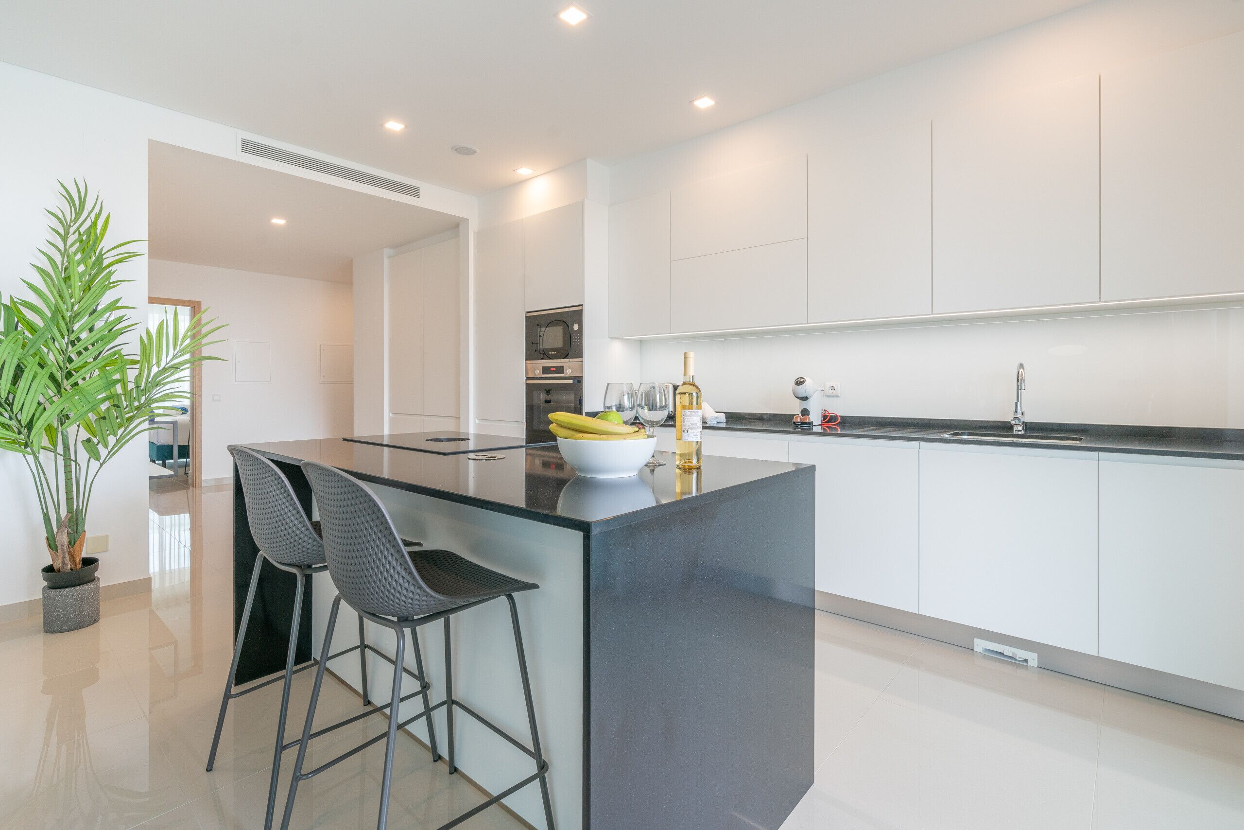 A modern kitchen with a central island, bar stools, a microwave, and a sink.