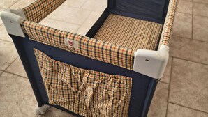 Una cuna para bebé con estampado escocés y ruedas, sobre un piso de baldosas.