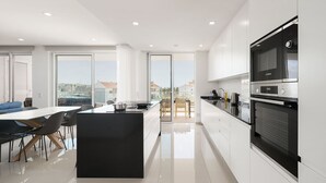 A modern kitchen with a large island, a dining area with chairs, and a view of the city through large windows. - Lagos Marina View 1 With Pool by Homing (Lagos)