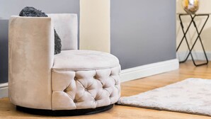 Un pouf capitonné avec une base noire, placé sur un plancher en bois, adossé à un mur gris.