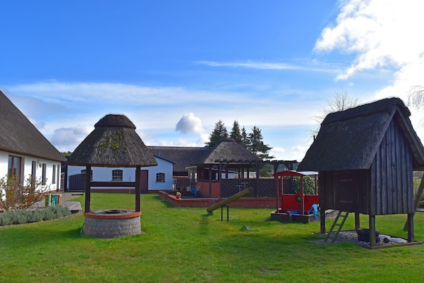 A rural village with thatched-roof structures, a playground, and a well-maintained grassy area.