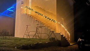 Un edificio blanco con una escalera que sube a un balcón, decorado con luces de adorno y guirnaldas.