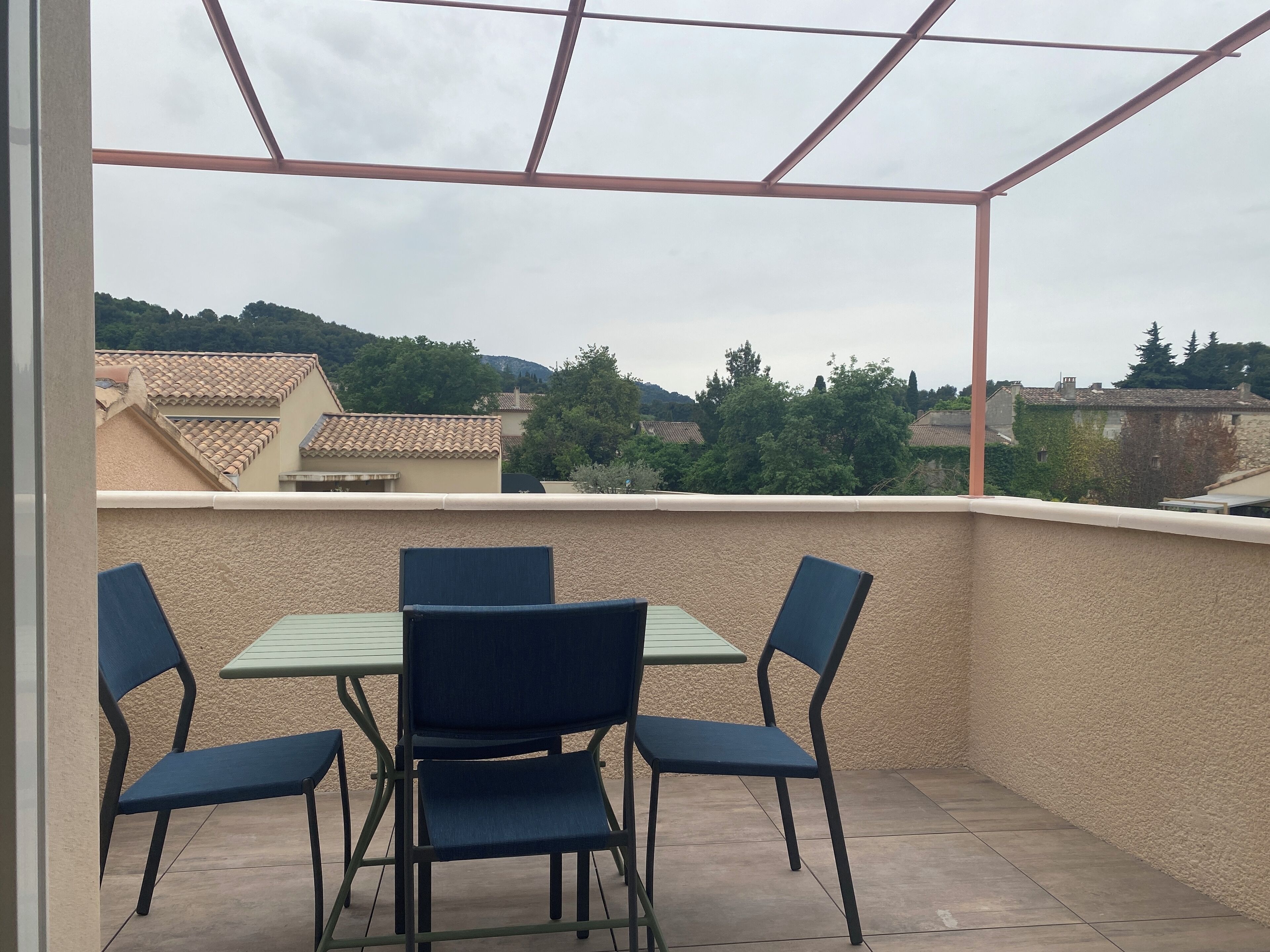 Varanda com mesa e cadeiras, vista para uma área residencial com casas e árvores.