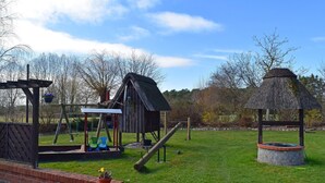 A playground with a swing set, a small wooden structure, and a thatched-roof gazebo. - Ferien unterm Reetdach bis zu 6 Personen (Alt Bukow OT Bantow)