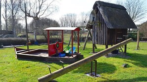 A playground with a seesaw, a red play structure, and a thatched-roof building. - Ferien unterm Reetdach bis zu 6 Personen (Alt Bukow OT Bantow)