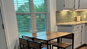 Eine Küche mit einem Holztisch und Stühlen, einem Fenster mit Jalousien und einer Spritzschutzleiste mit sechseckigem Muster.