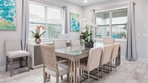 A modern dining room with a glass table, six chairs, and two large windows with curtains. - Luxury Retreat  7Bd Home - Close to Disney (Kissimmee)