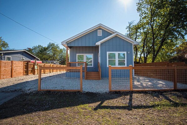 A small, single-story building with a blue exterior and white trim, surrounded by a wooden fence and gravel ground. - Stylish 3br/2ba Urban Retreat Near Lively Downtown (San Antonio)