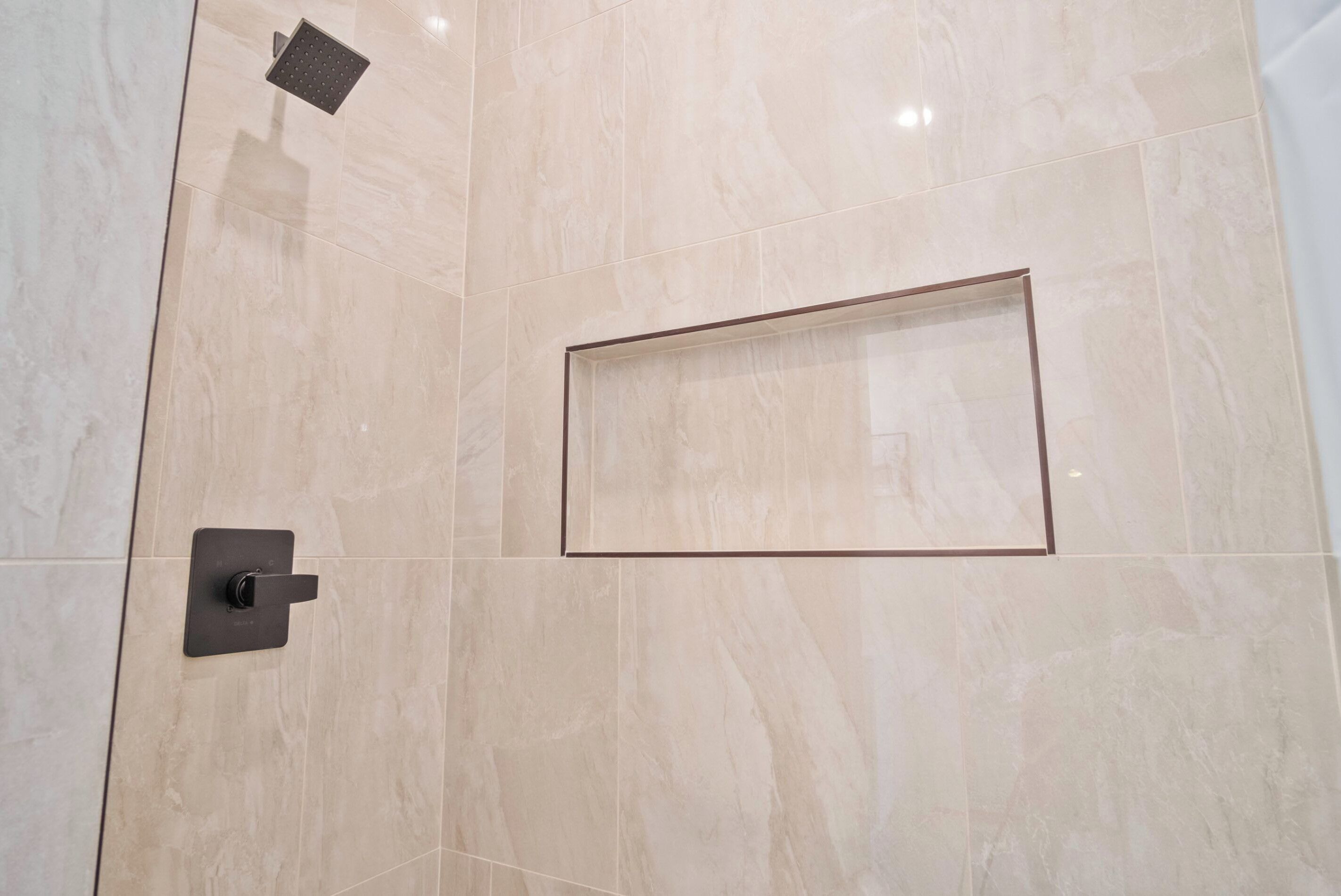 Een badkamer met een grote spiegel, een douchekop en een rechthoekig wastafelgedeelte.