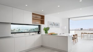A modern kitchen with a large window, a dining area with chairs, and a view of the city. - Lagos Deluxe 1 With Pool by Homing (Lagos)