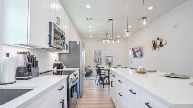 A modern kitchen with white cabinetry, a central island, and a dining area with a table and chairs. - Feel, Chill and Enjoy 4br/3ba Near Fun Riverwalk! (San Antonio)