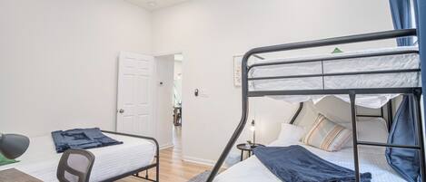 A dormitory room with bunk beds, a desk, a chair, and a ceiling fan.