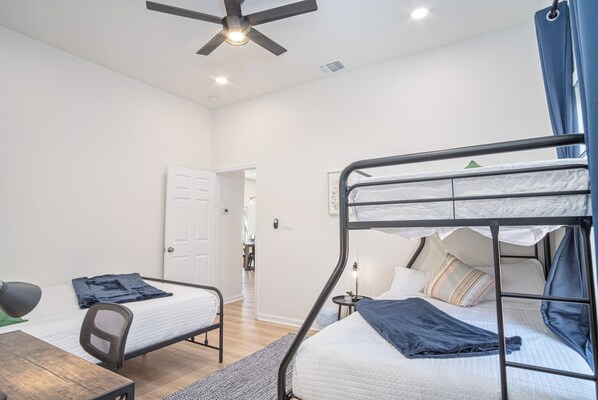 A dormitory room with bunk beds, a desk, a chair, and a ceiling fan.