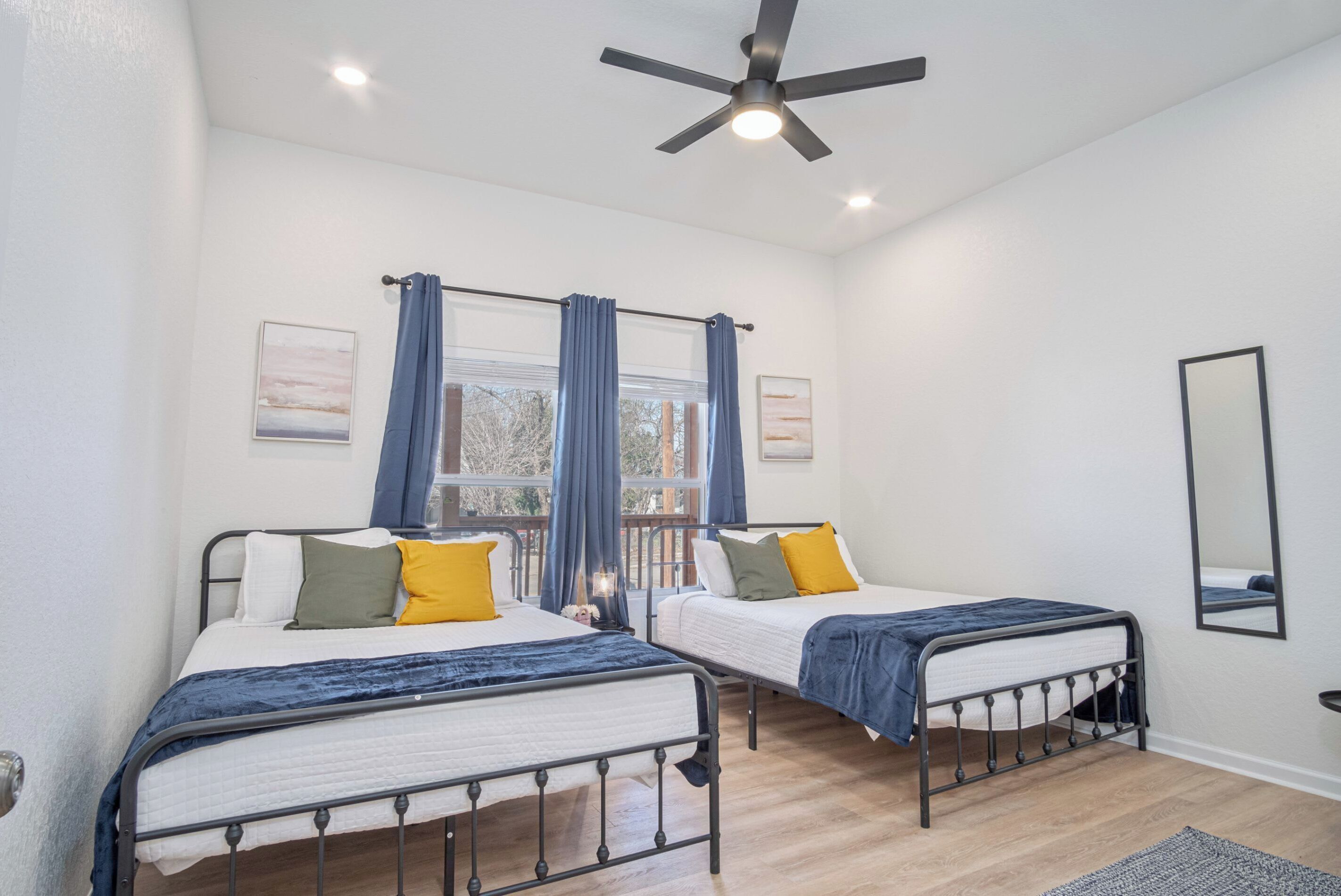 A bedroom with two beds, a ceiling fan, and a window with curtains.