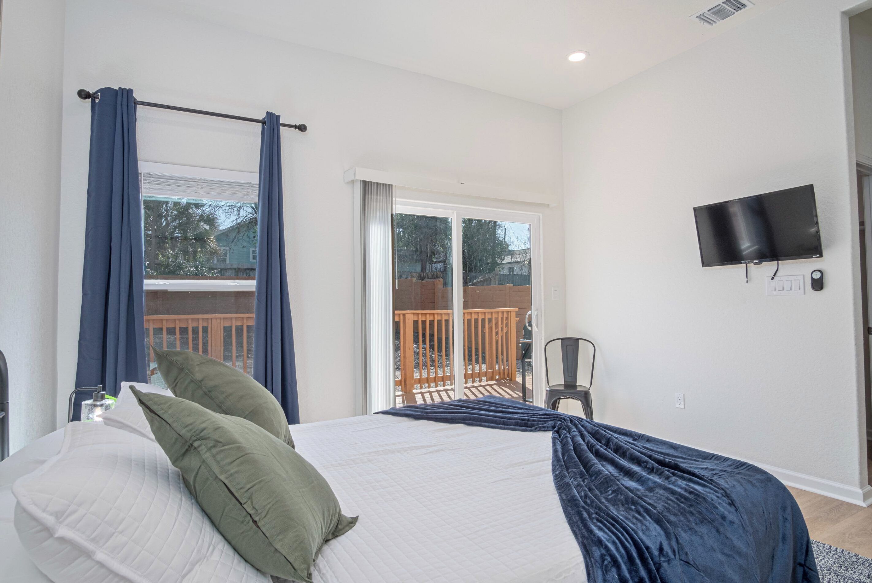 A bedroom with a bed, curtains, a TV, and a balcony with a railing.