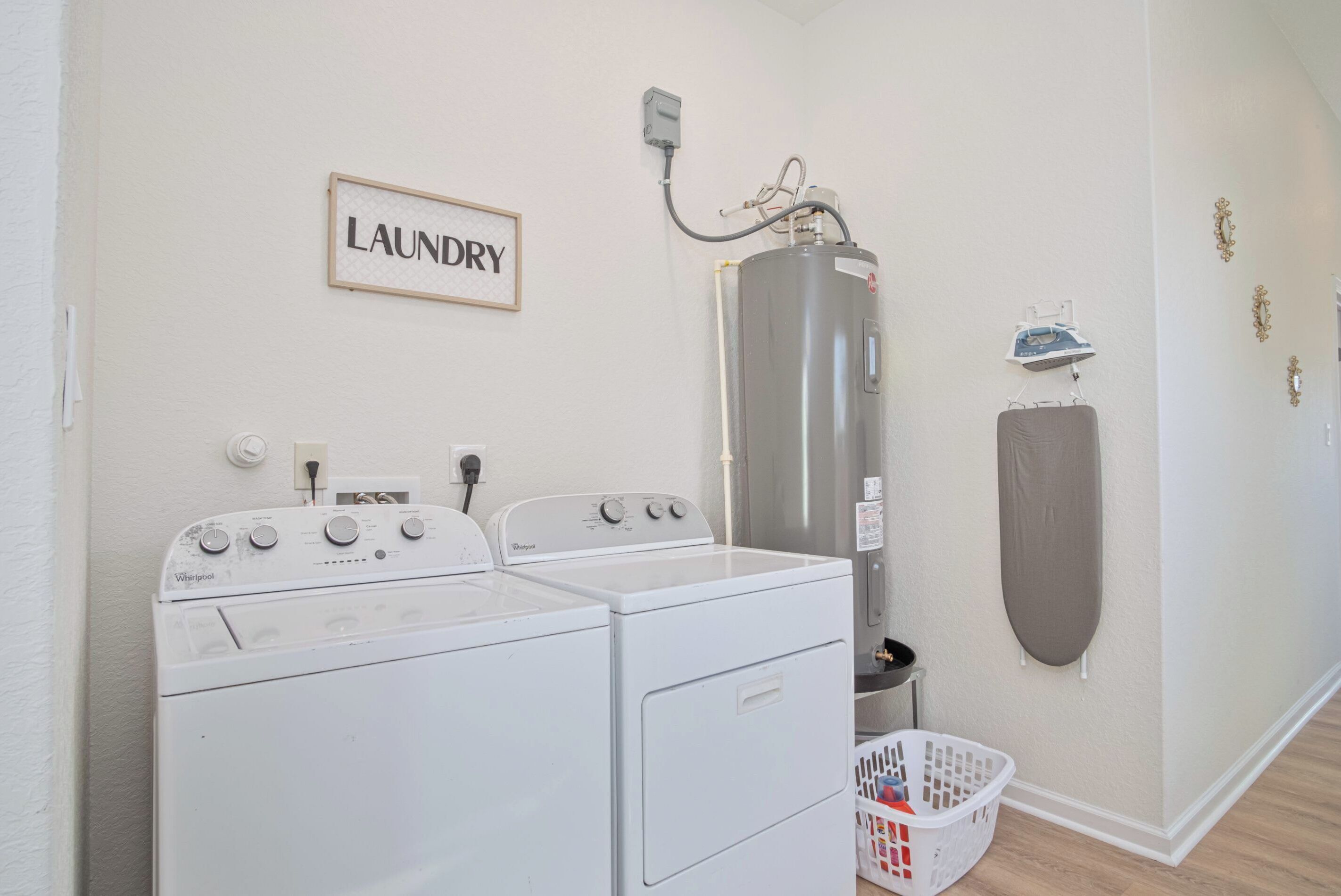 A laundry area with two front-loading washers, a tall water heater, and a wall-mounted ironing board.