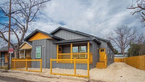 A modern two-story house with a grey exterior, a wooden deck, and a fenced front yard.