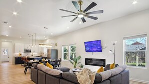 A modern living room with a grey sectional sofa, a flat-screen TV mounted on the wall, and a dining area with a kitchen in the background.