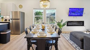 A modern kitchen with a stainless steel refrigerator, a dining table set with white plates and bowls, and a chandelier.