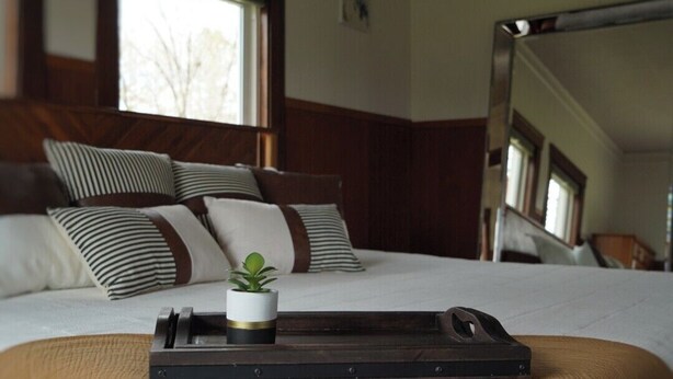 A neatly made bed with striped pillows, a small potted plant, and a tray on the bed. - Historic Whiffletree place, 4br, riverview, no neighbors (Sparland)