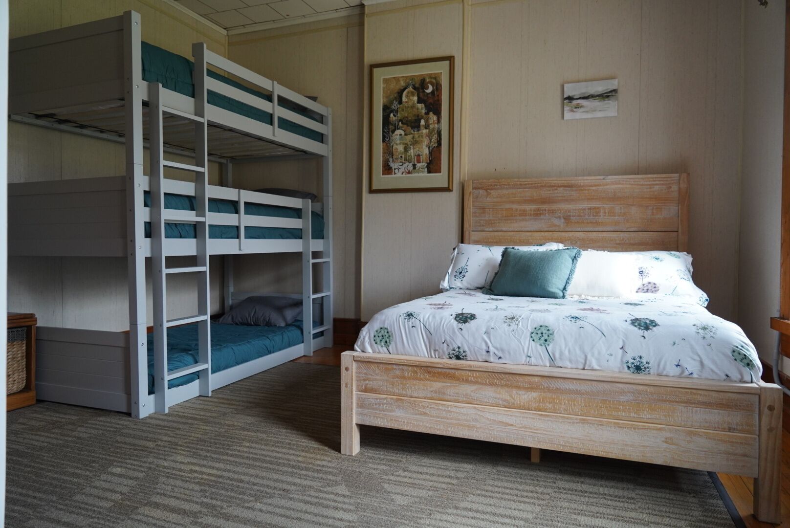 Een slaapkamer met een stapelbed, een enkel bed met bloemenbeddengoed, een ingelijst schilderij aan de muur, en een vloerbedekt met tapijt.