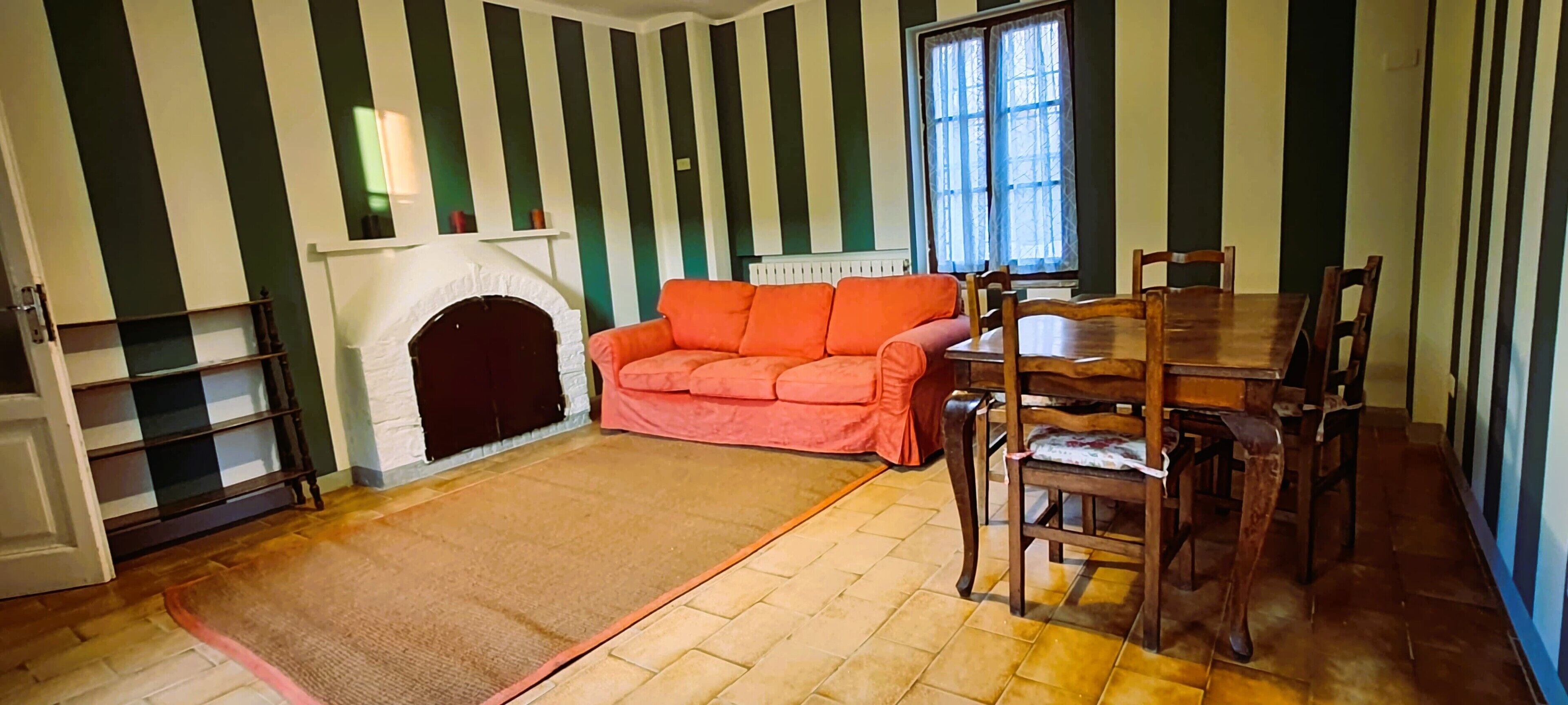 Una habitación con chimenea, un sofá, una mesa de comedor con sillas y una pared a rayas.