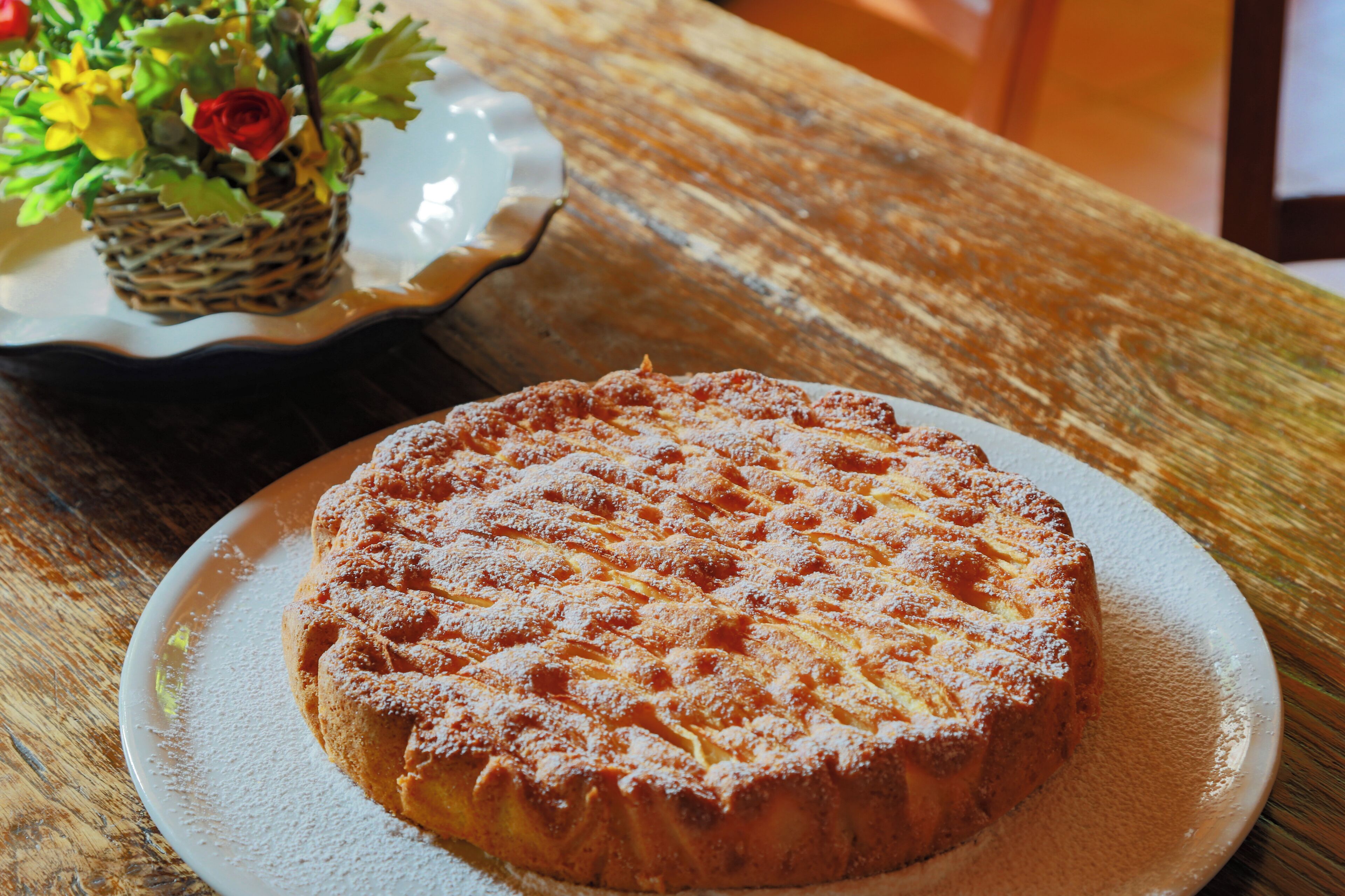 A round cake with powdered sugar on a white plate, placed on a wooden table.