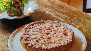 Bolo redondo com açúcar espolvorado sobre um prato branco, colocado em uma mesa de madeira.