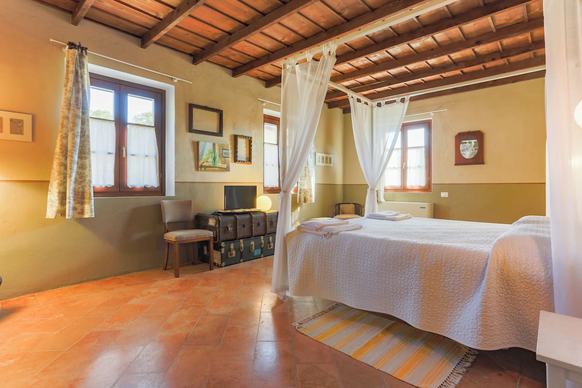 A bedroom with a bed, a suitcase, a chair, and a window with curtains.
