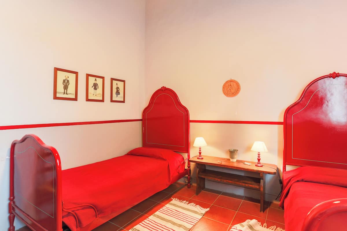 A room with two red beds, a wooden nightstand with two lamps, and three framed pictures on the wall.