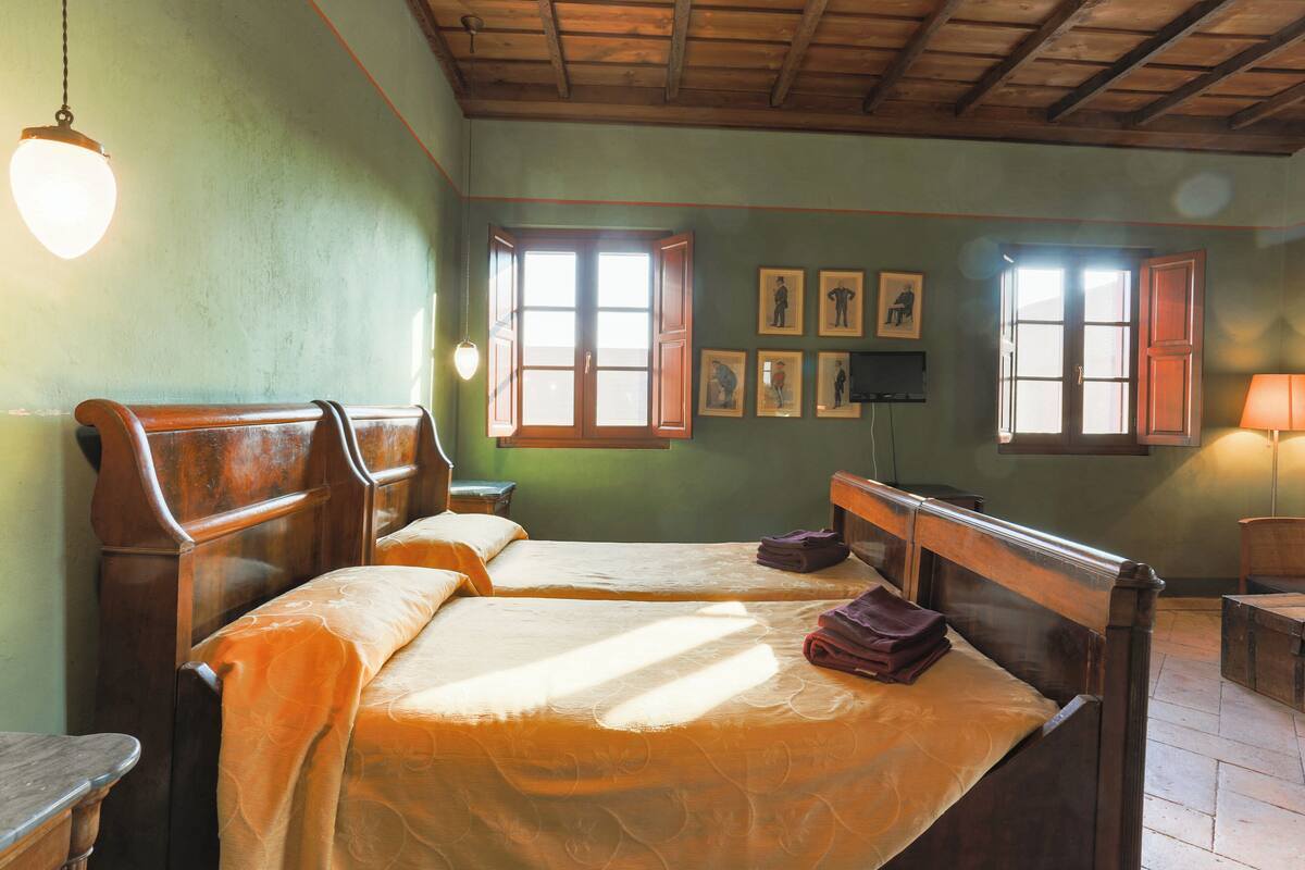 A room with two wooden beds, a wooden desk, a chair, and a lamp.