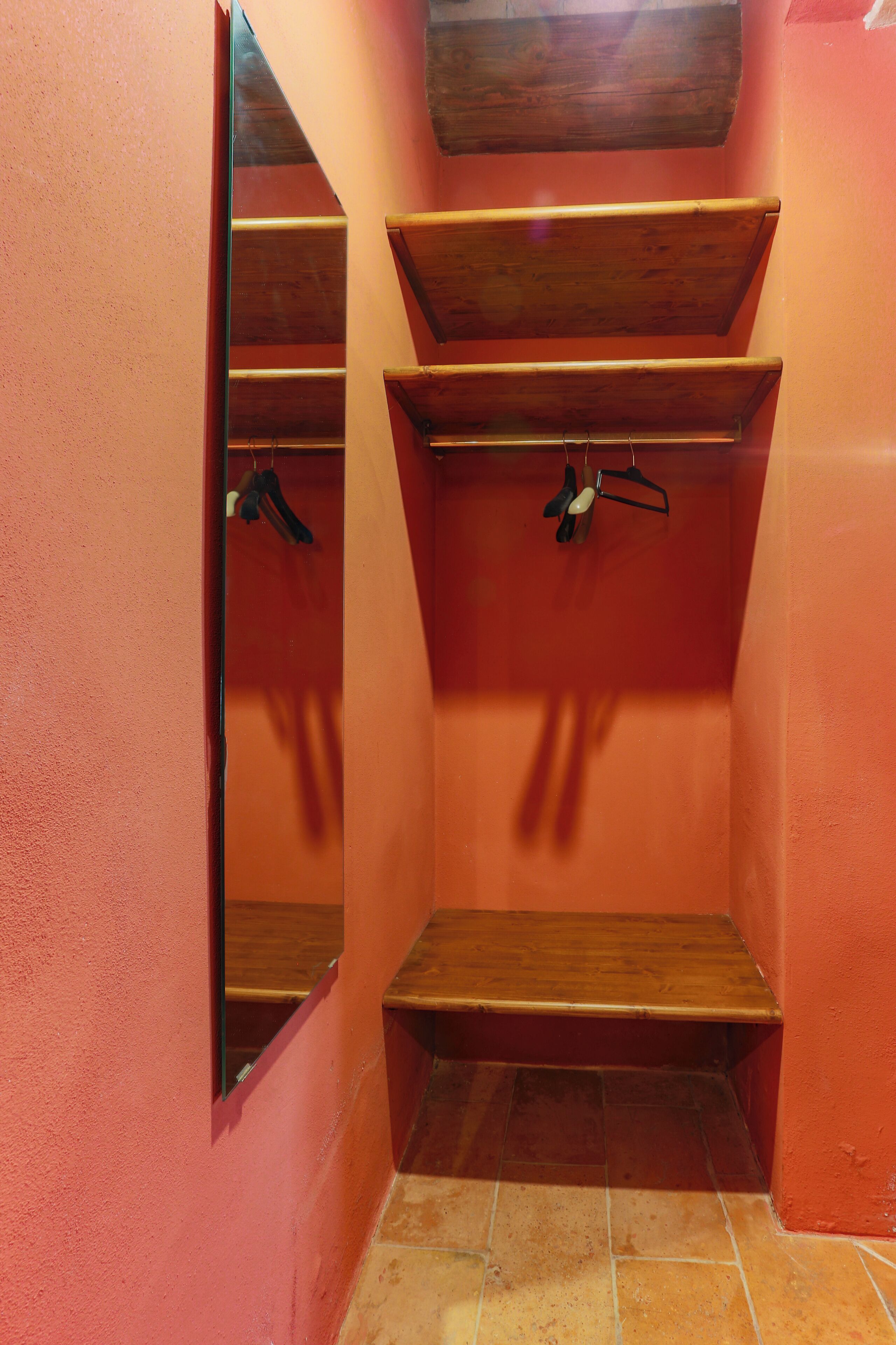 Une petite pièce fermée, avec un banc en bois, un miroir et une étagère où sont accrochés divers objets.
