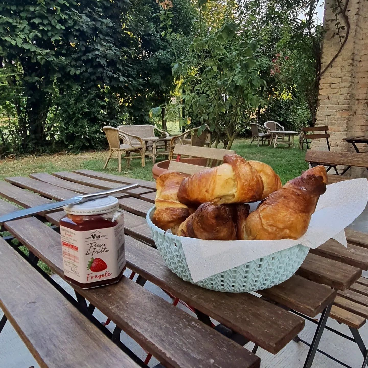 Une table de pique-nique avec un panier de croissants et un pot de confiture de fraises.