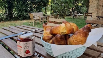 Une table de pique-nique avec un panier de croissants et un pot de confiture de fraises.