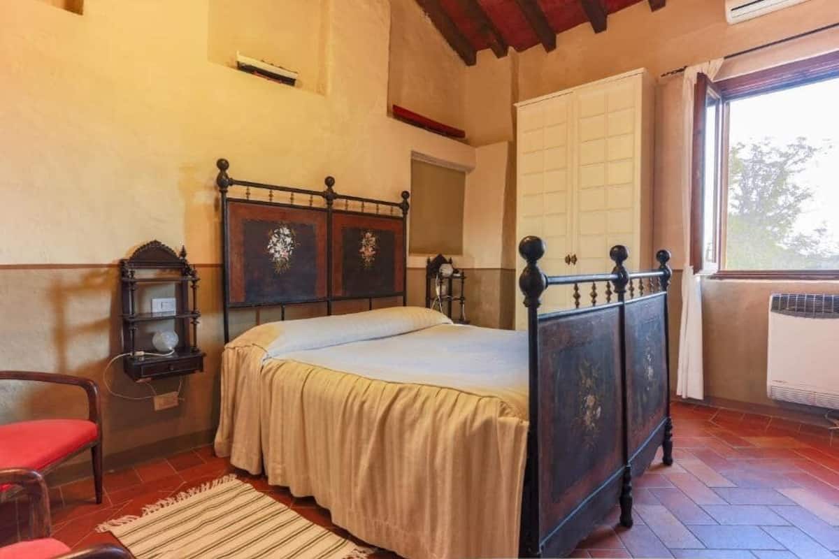 A bedroom with a wooden bed, a nightstand, a chair, and a window with a view.