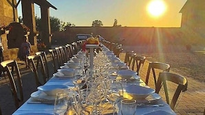 A long table set for a meal with chairs on both sides, under a clear sky with the sun low on the horizon. - AGRITURISMO LE CORTI DELLA GUALDANA (Voghera)