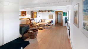 A spacious living area with a sofa, a chair, a table, and a fireplace. There are bookshelves and artwork on the walls. - 4 Star Holiday Home in Laeso (Læsø)