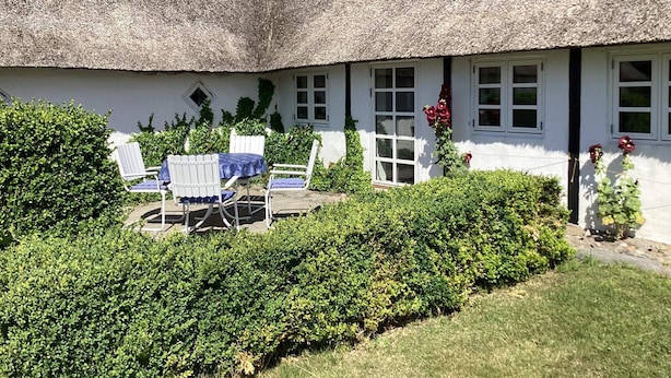 A thatched-roof cottage with a small patio area, white walls, and a garden. - 4 Star Holiday Home in Laeso (Læsø)