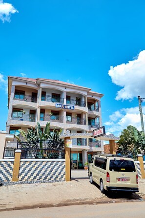 Un hôtel à plusieurs étages doté de balcons, un fourgon garé devant, et un ciel bleu dégagé.