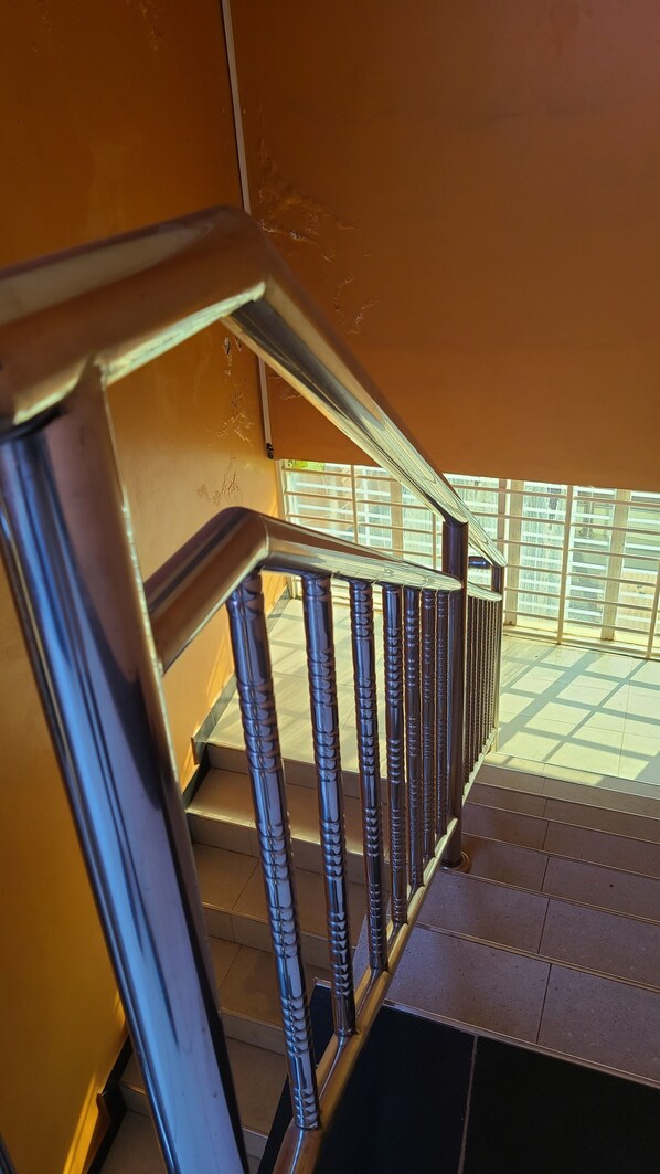Un escalier avec une rampe en métal menant à un espace baigné de lumière, d’où l’on peut admirer la façade d’un immeuble.