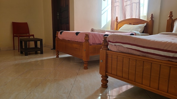 A bedroom with two wooden beds, a small wooden chair, and a tiled floor. - Muju Hotel Mbarara (Mbarara)