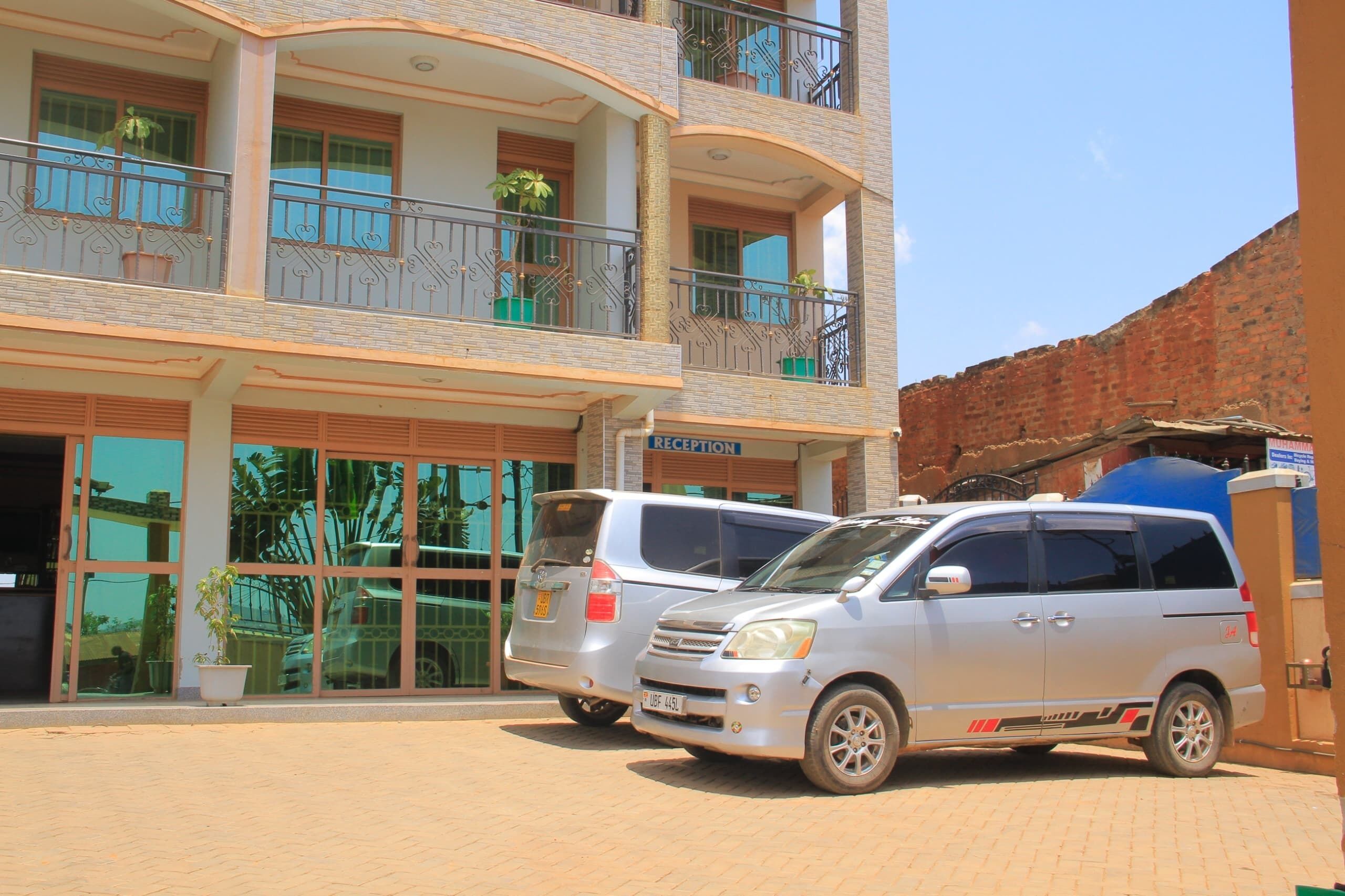 A multi-story building with a reception area, two parked cars, and potted plants on balconies.