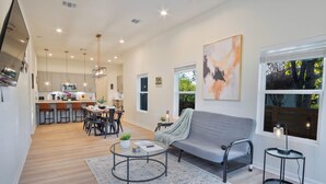 A modern living room with a grey sofa, a coffee table, and a dining area with chairs and a table.